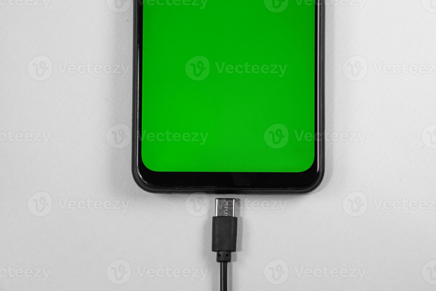 mobile phone with green screen connected to a charger on white background photo