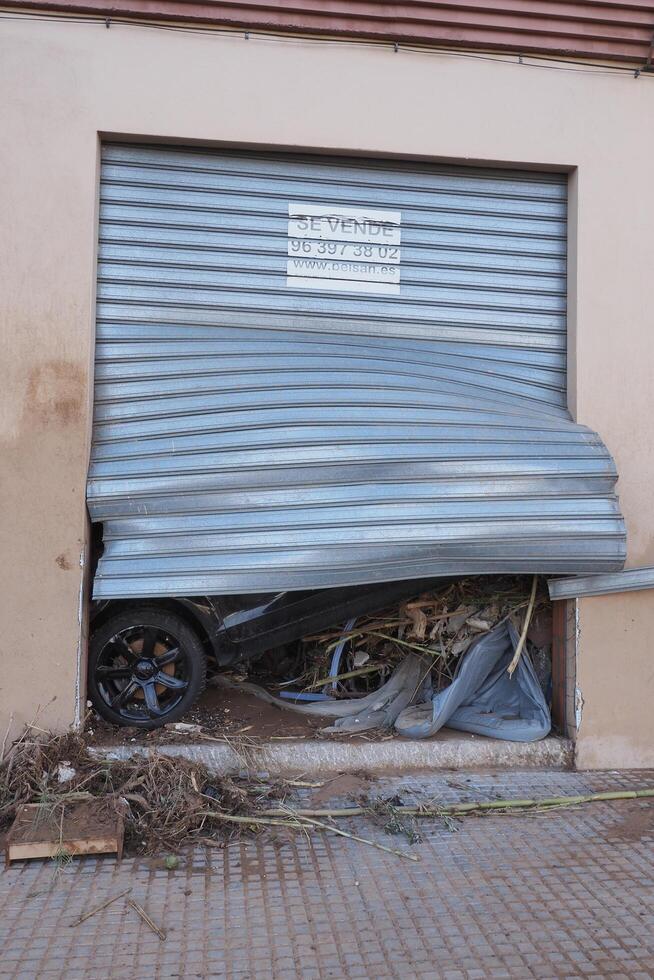 VALENCIA, SPAIN OCTOBER 31, 2024. Broken garage door revealing a damaged car, consequence of the devastating floods in Valencia photo