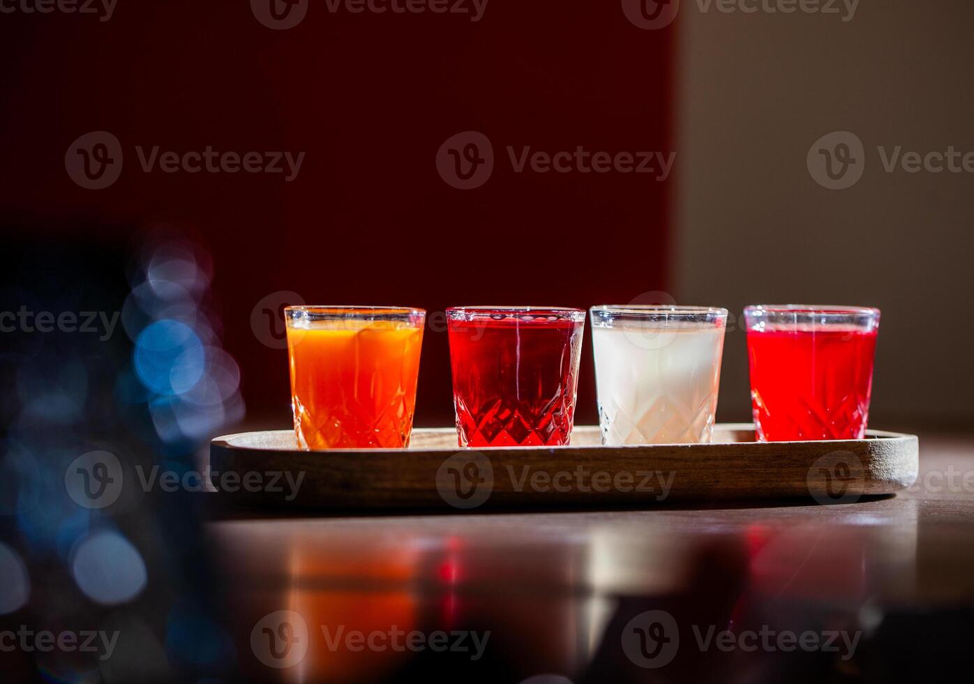 Four colorful shots of alcoholic beverages are placed on a wooden tray, creating a vibrant and inviting scene photo