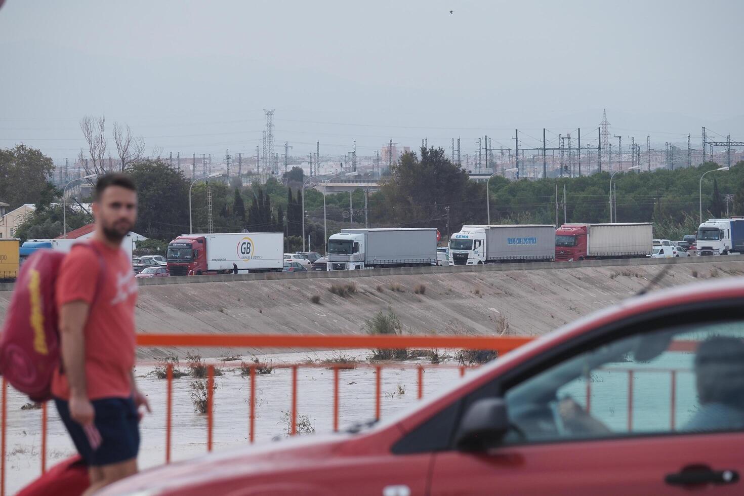 VALENCIA, SPAIN OCTOBER 31, 2024. Trucks stuck in traffic jam next to flooded river in Valencia, Spain, showcasing the impact of climate change and extreme weather photo