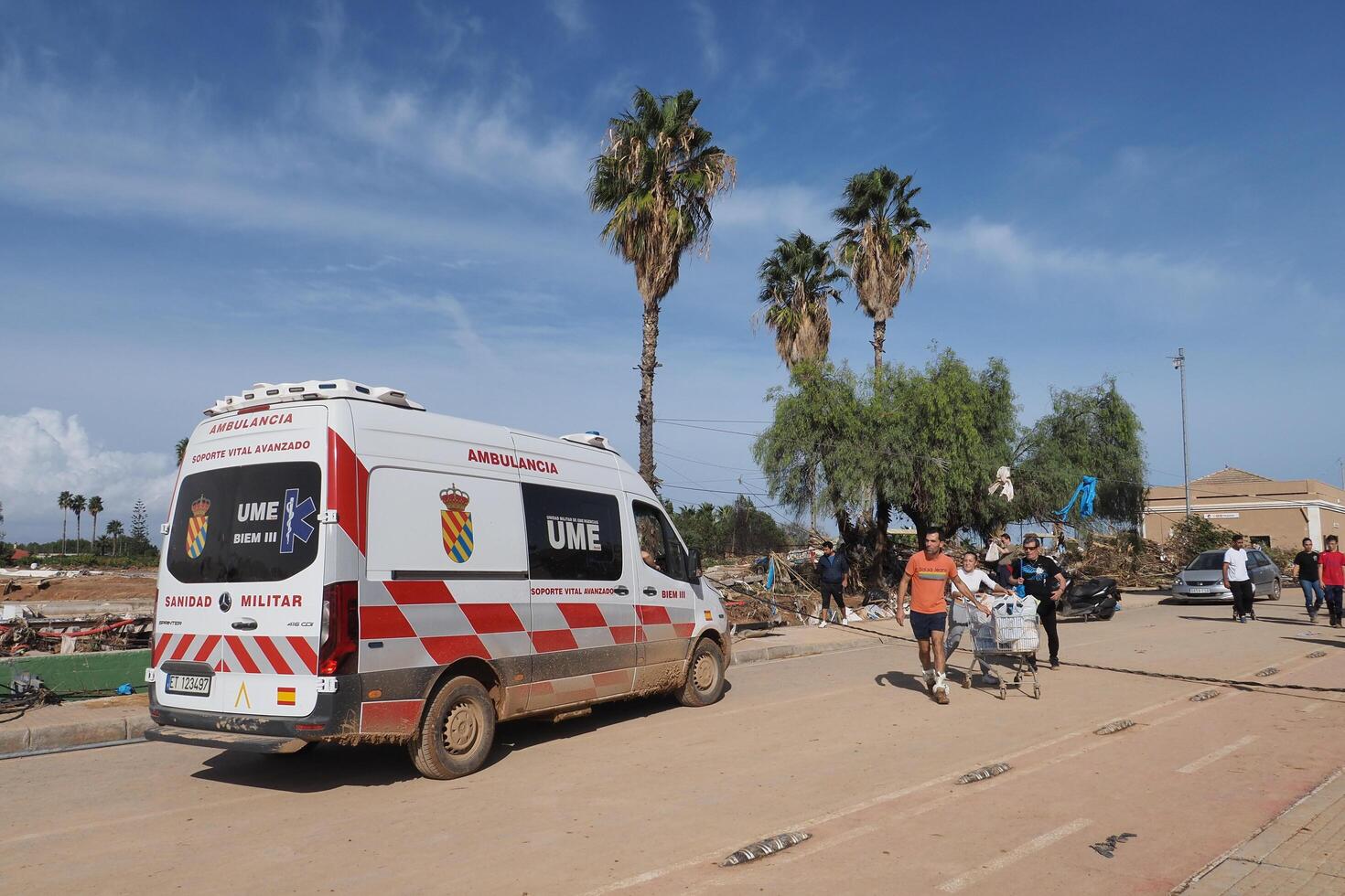VALENCIA, SPAIN OCTOBER 31, 2024. Residents pushing shopping cart with belongings, seeking help near a military ambulance after devastating floods in Valencia photo