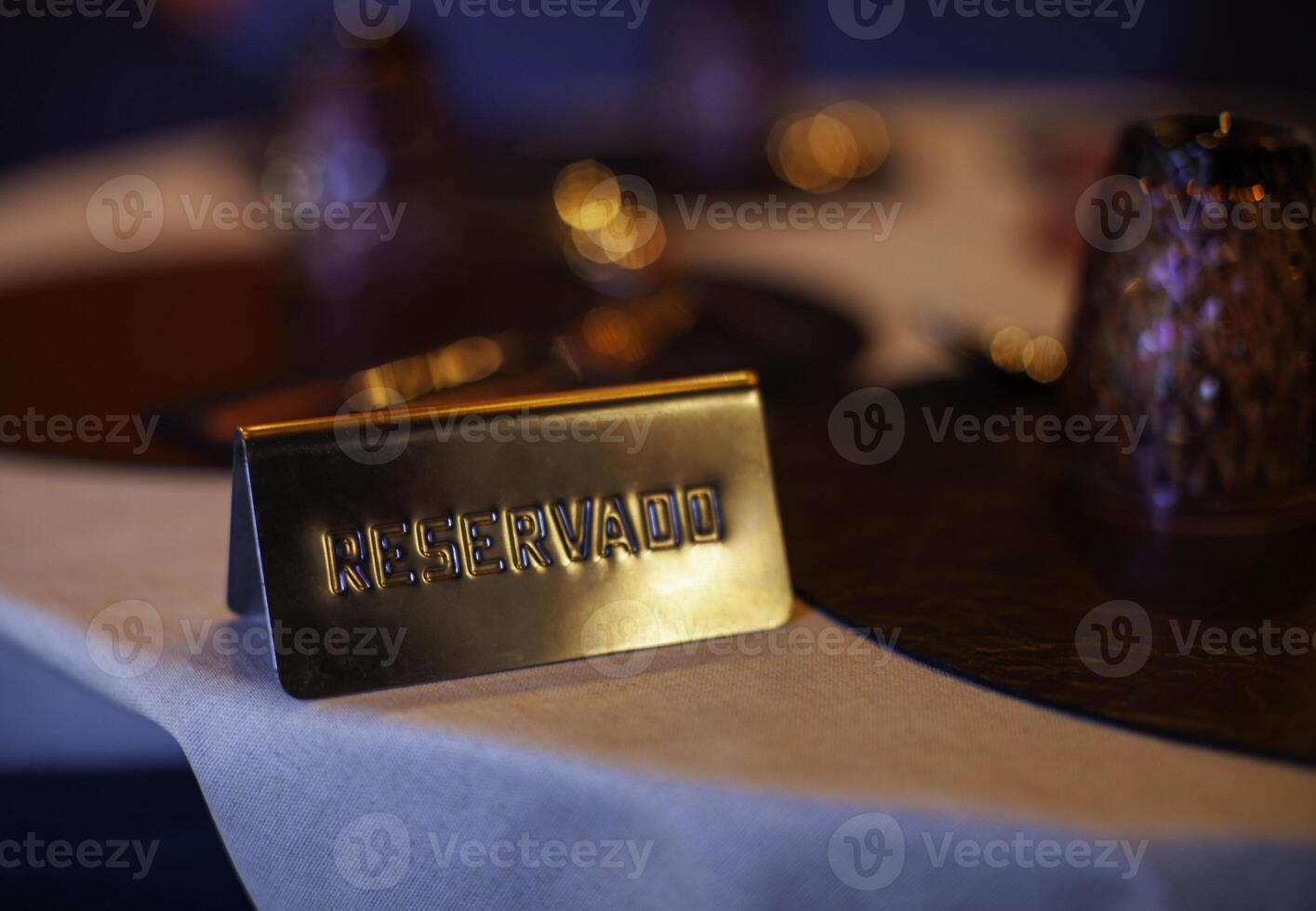 Golden reserved sign placed on restaurant table, indicating a prior booking, amidst ambient lighting and table settings photo