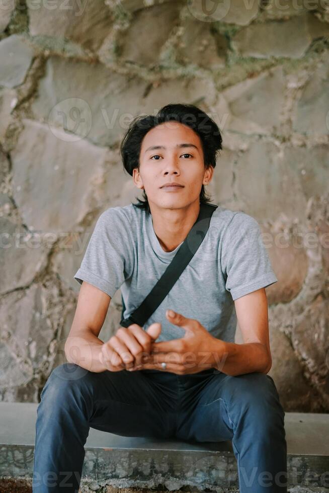 Southeast Asian man sitting with a neutral, expressionless face, looking straight ahead photo