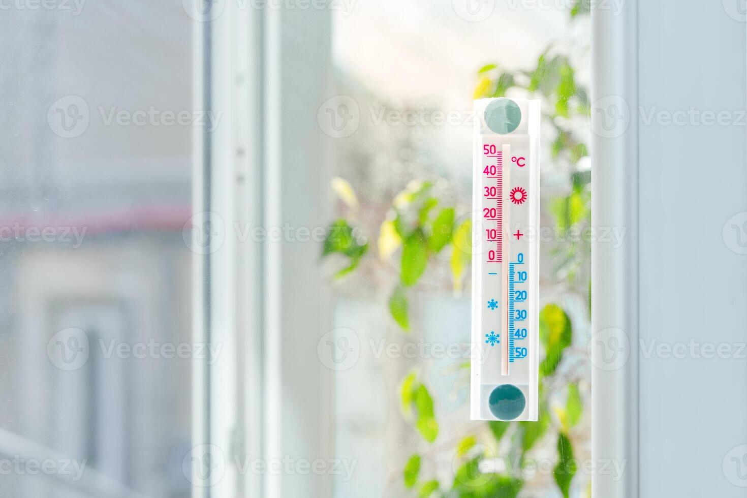White Plastic Thermometer Attached to a Window With a Plant in the Foreground photo