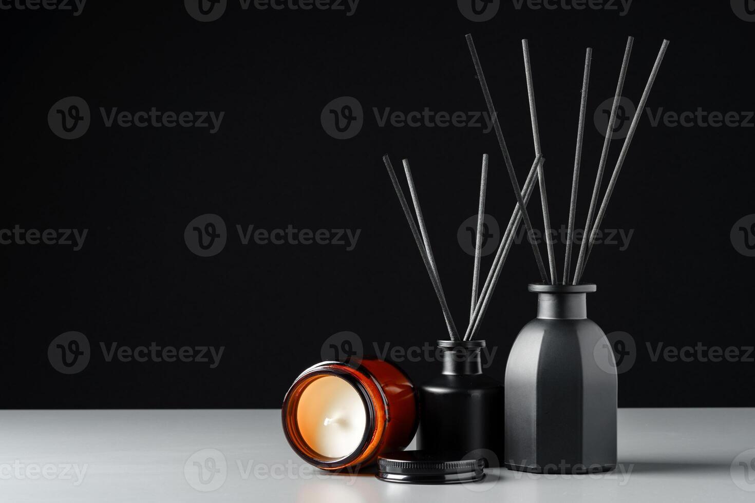Black Reed Diffuser and Candle on Grey Surface Against Black Background photo