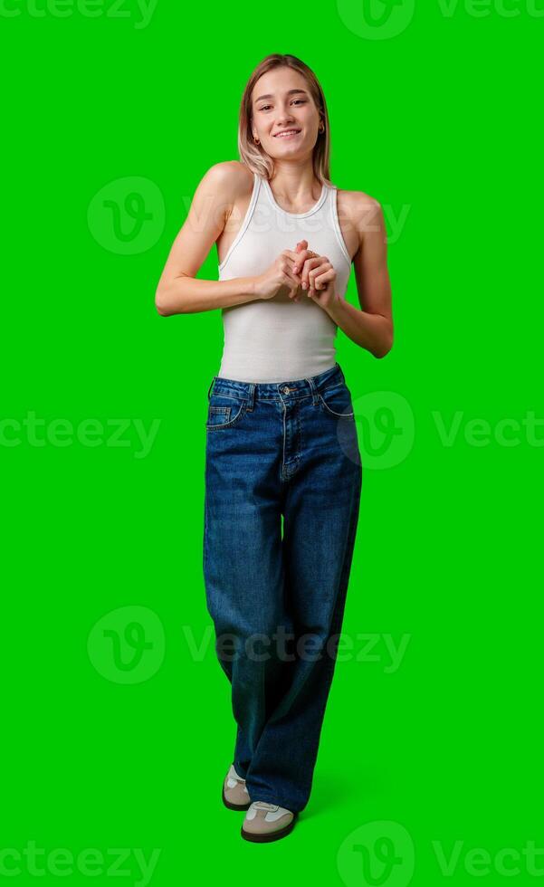 Young Woman Wearing White Tank Top and Blue Jeans Poses Against Green Screen photo