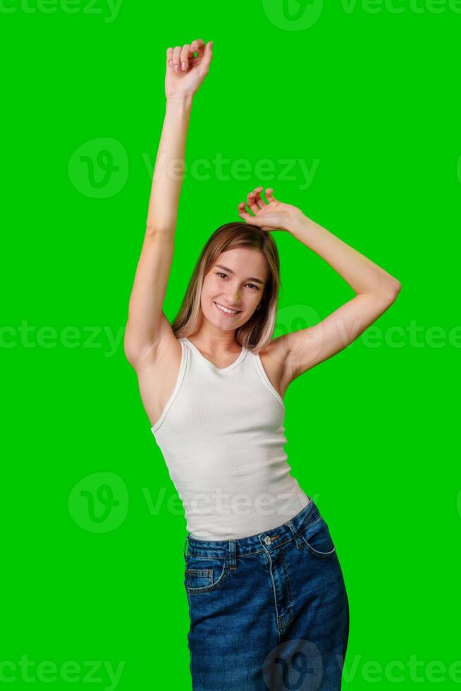 Young Woman Dancing in White Tank Top and Jeans Against Green Screen photo