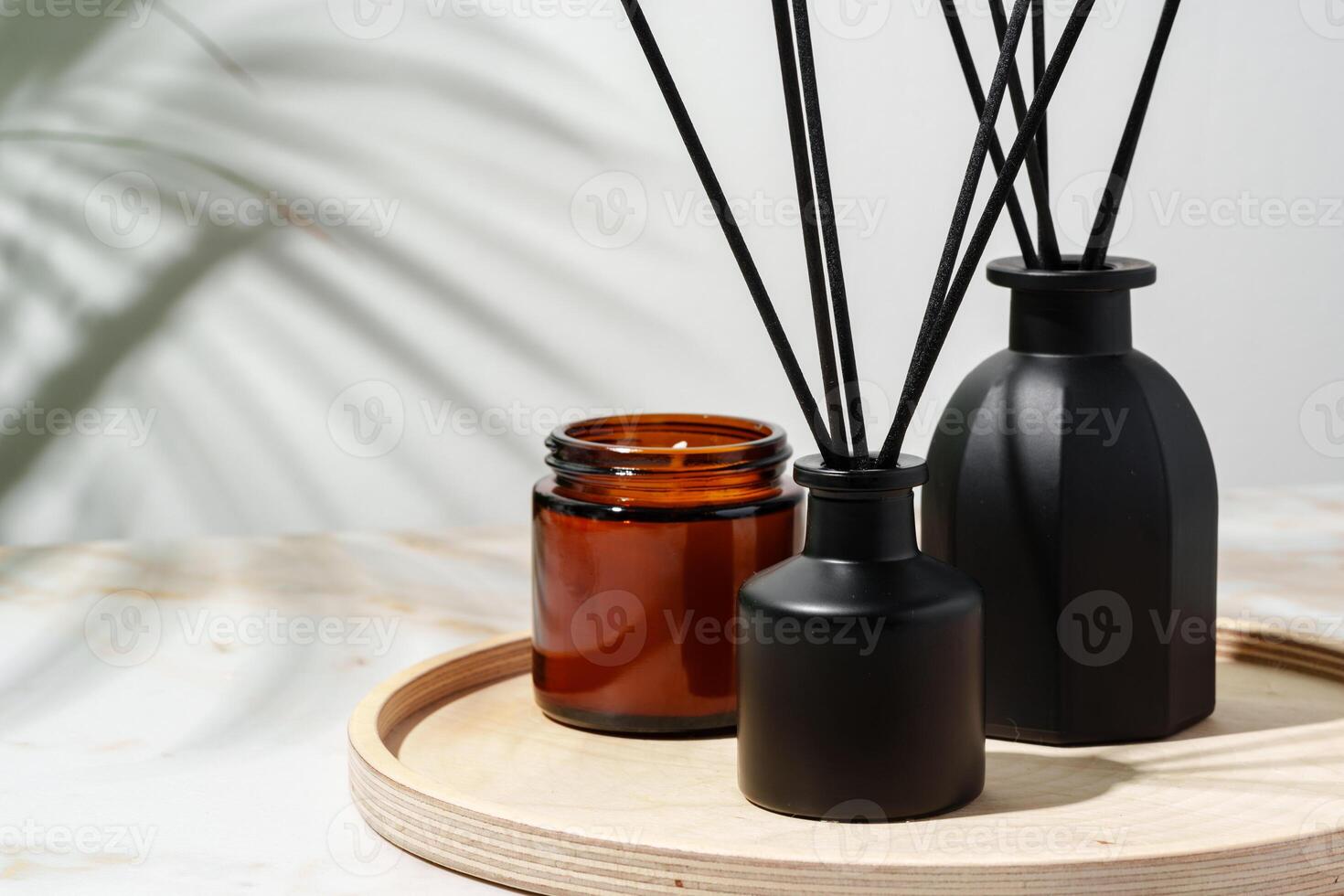 Black Reed Diffuser, Amber Candle, and Wooden Tray on White Surface photo