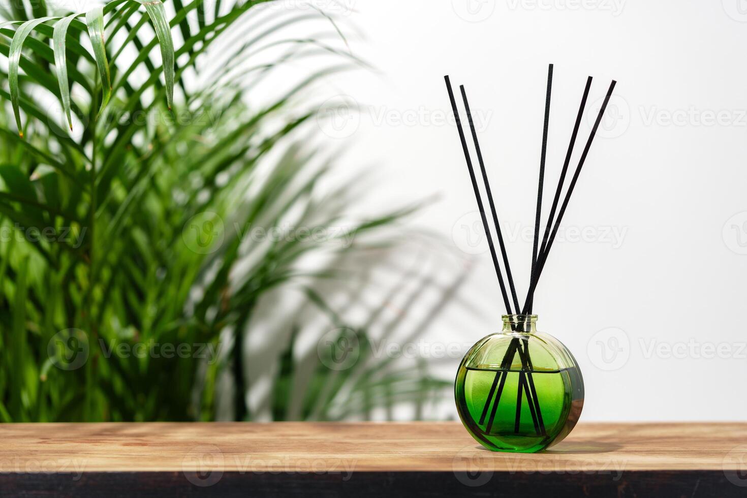 Green Glass Reed Diffuser On Wooden Tabletop With Greenery In Background photo