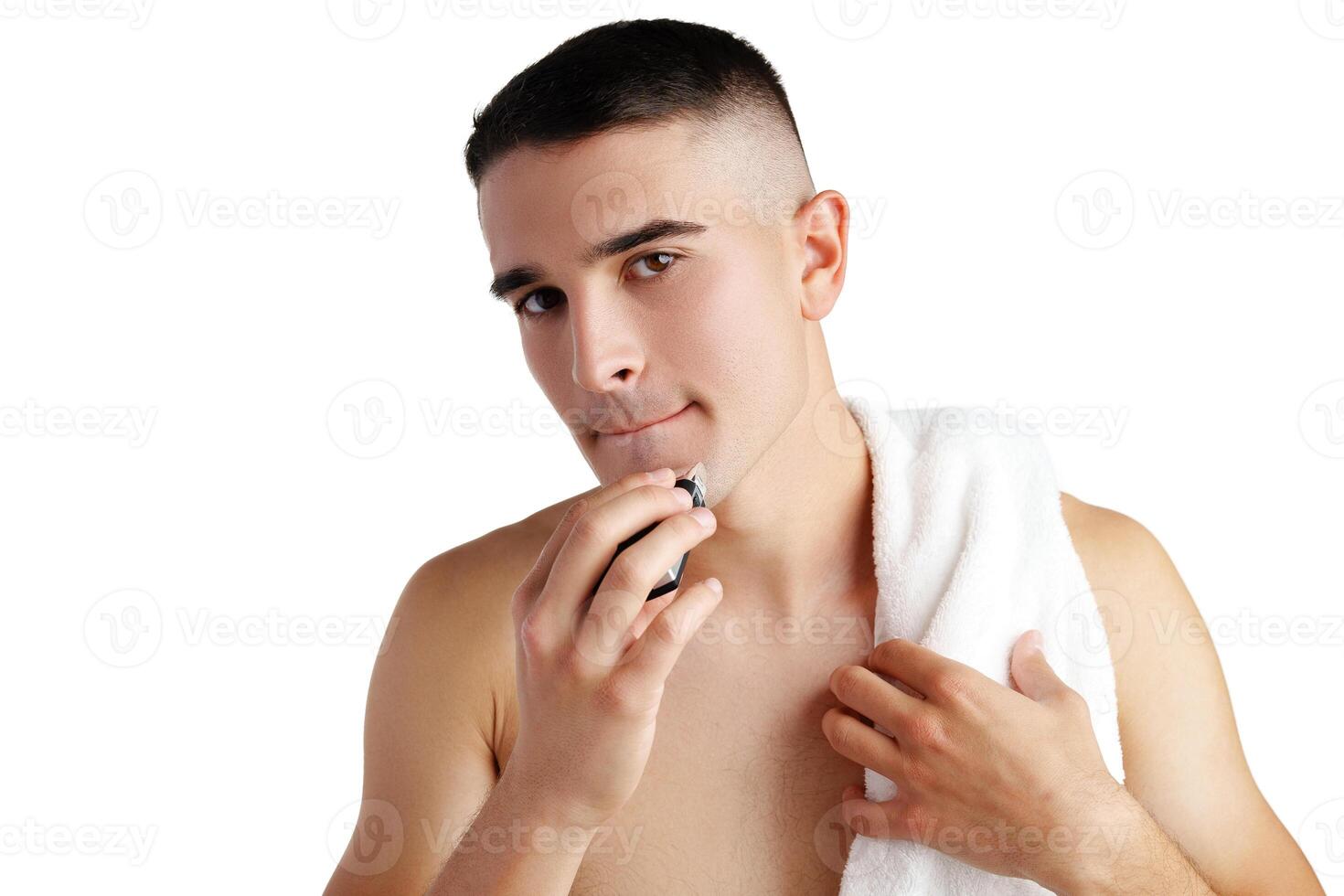 Handsome young man shaving face with electric razor on white background photo