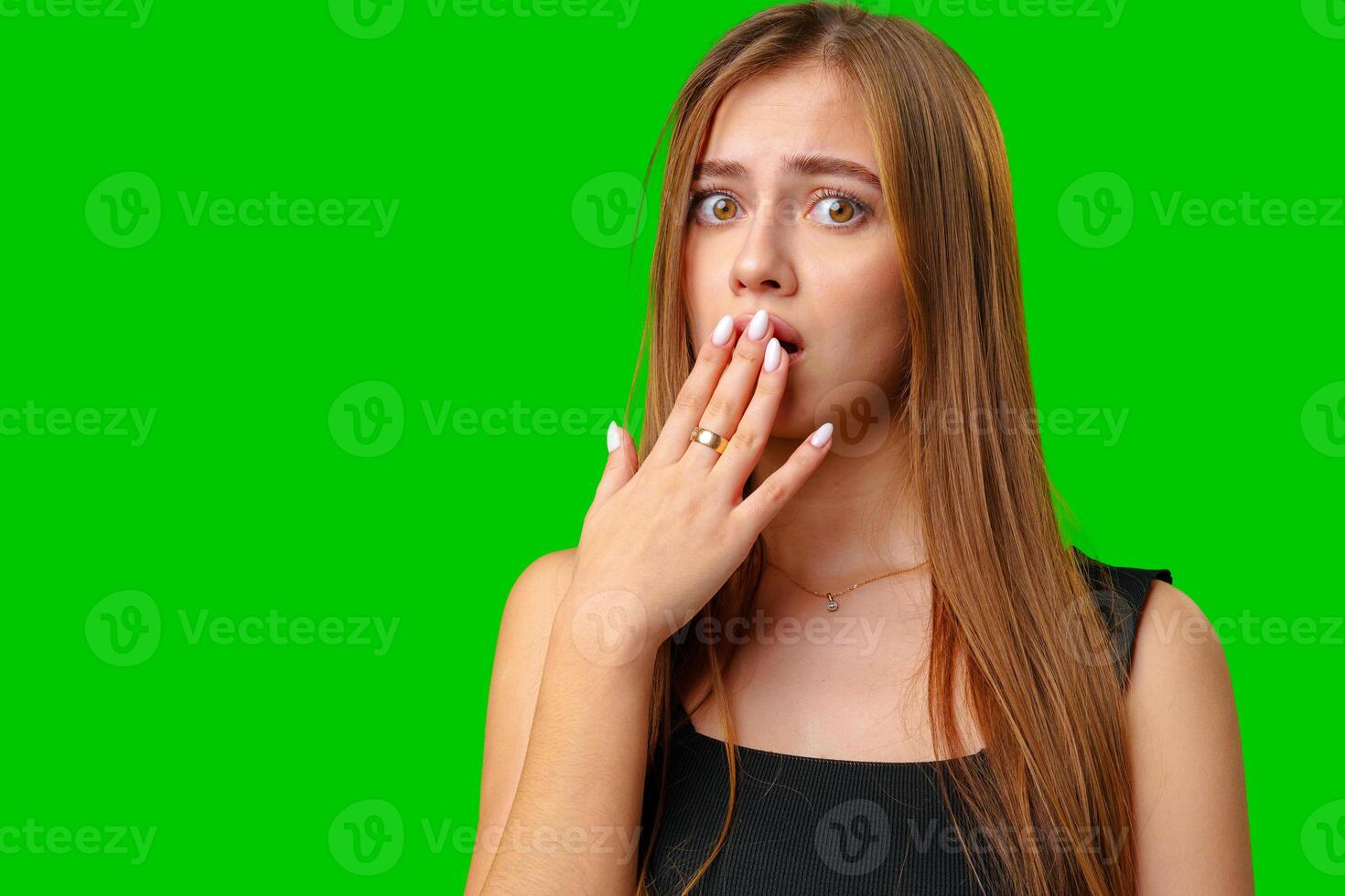 Young Woman Covering Mouth With Hand in Shock Against Green Screen photo