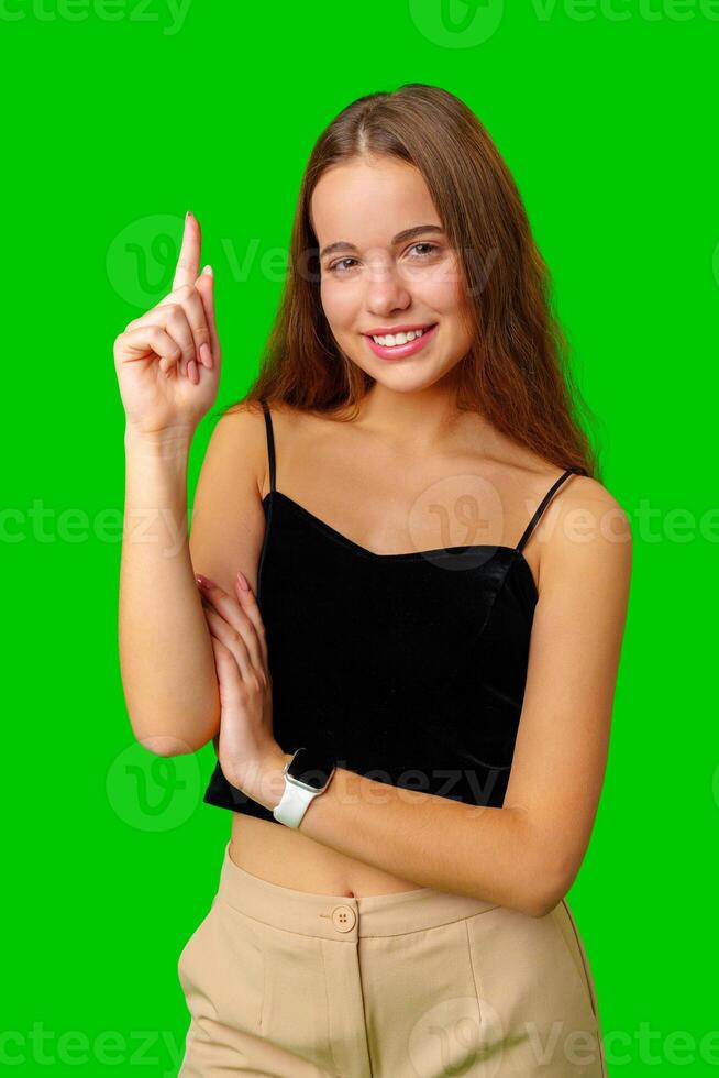 Smiling Woman Pointing Upwards Against a Green Screen Background photo
