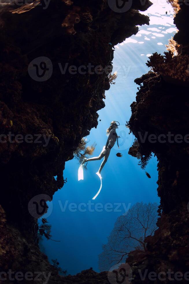 Woman freediver diving in underwater cave with rocks on Menjangan island, Bali. photo