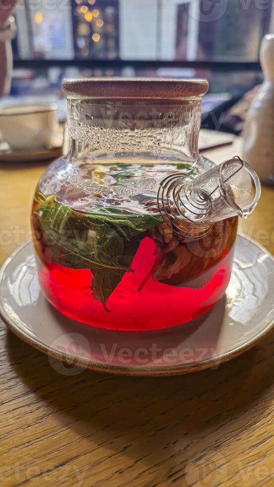 A teapot with hibiscus tea, mint leaves and walnuts. On a table in a cafe. photo