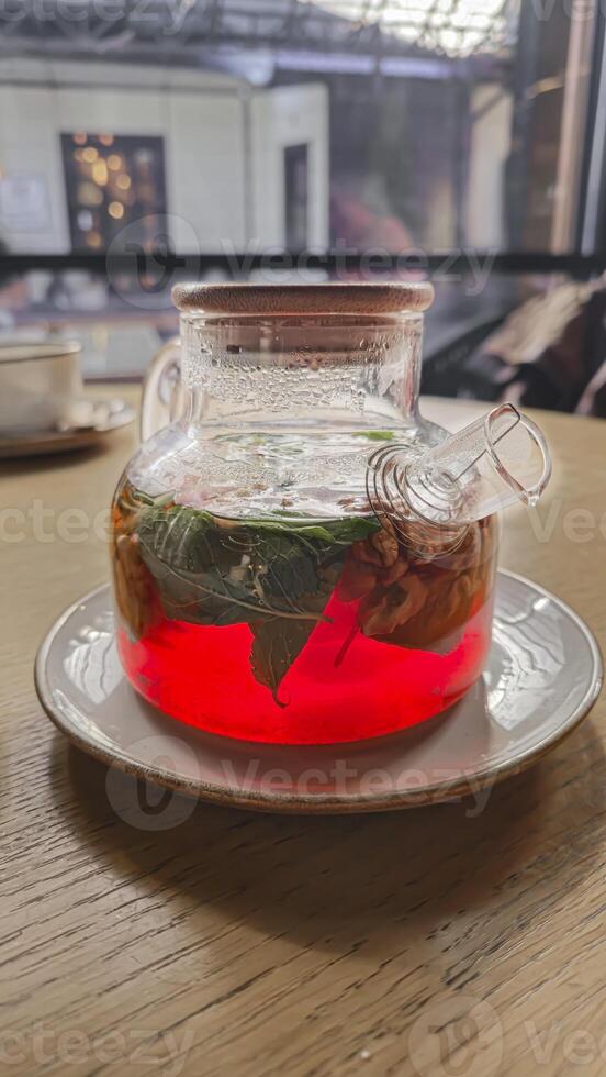 A teapot with hibiscus tea, mint leaves and walnuts. On a table in a cafe. photo