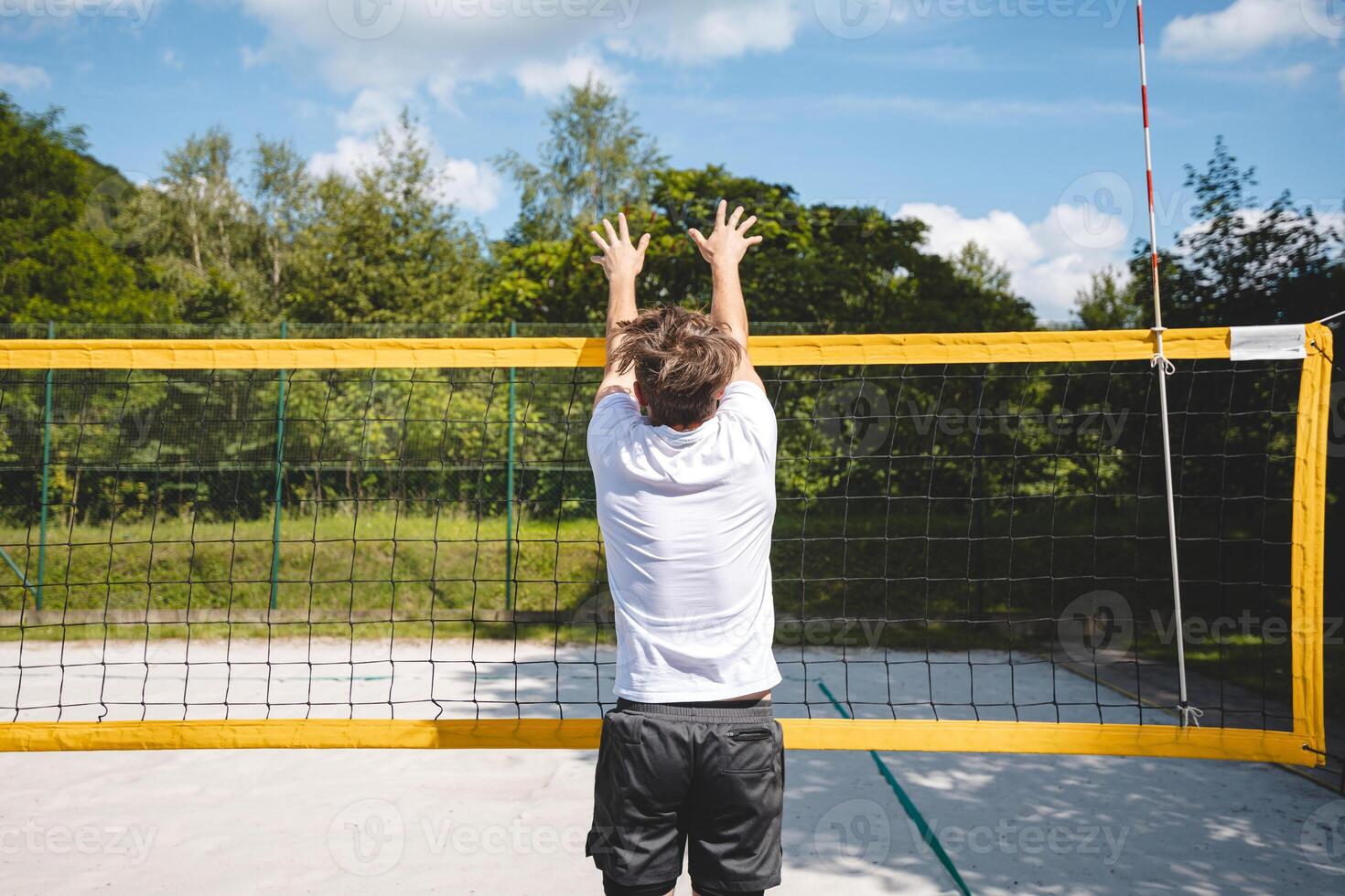 Volleyball player jumping to block a volleyball at the net on a sand court. The outdoor scene captures the intensity of summer sports and beach volleyball photo