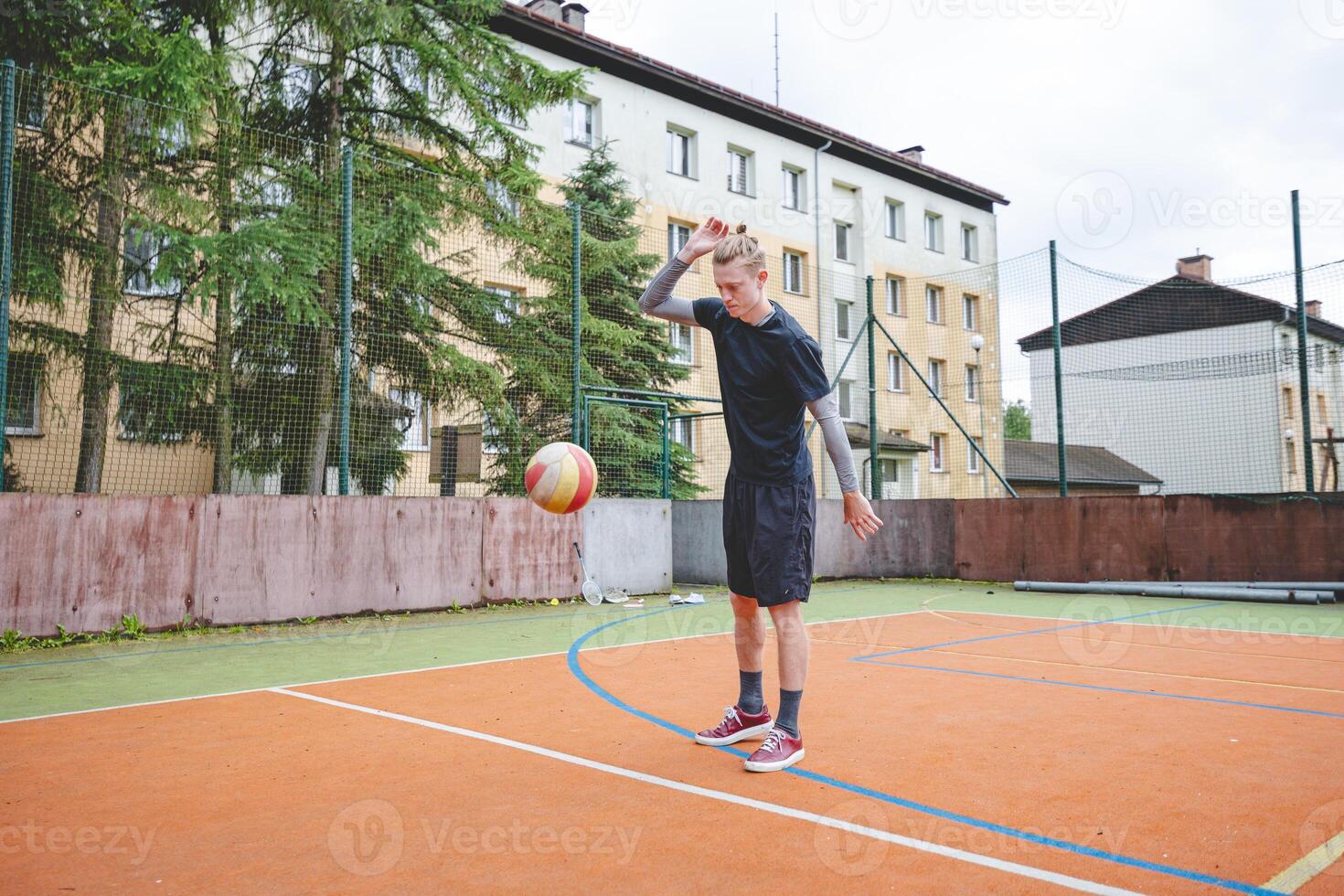 Volleyball player standing on a hard court, bouncing the ball while preparing for the next play during an outdoor game. A calm, focused moment before the action begins photo