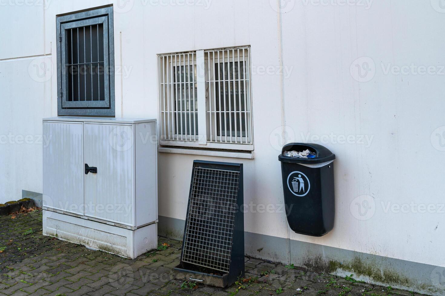 A gray utility storage unit stands beside a black waste bin attached photo