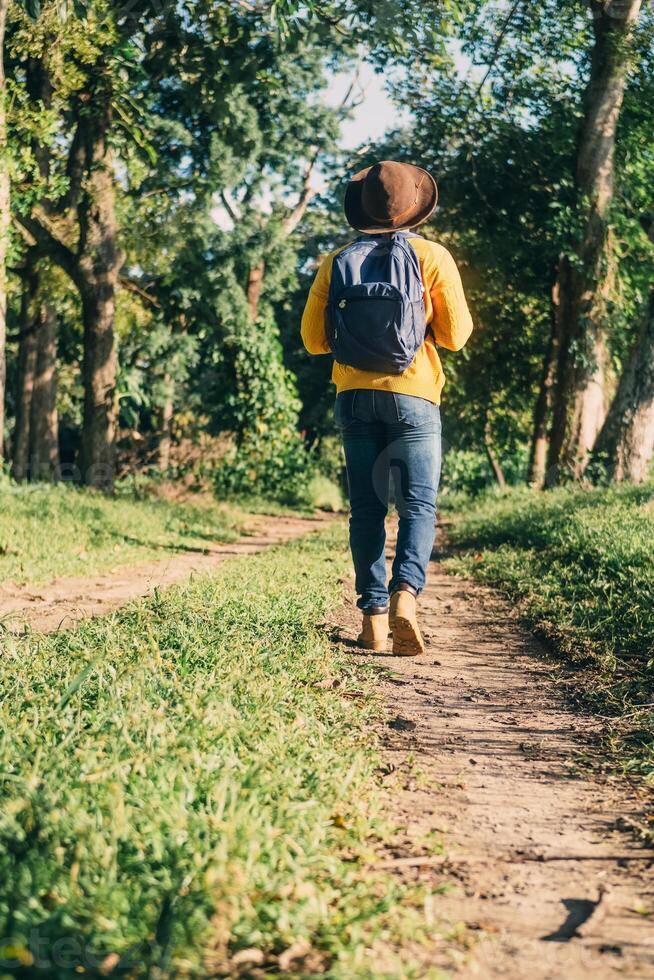 man with backpack boots and a hat walking on a path in a forest, nature travel and hiking concept. photo