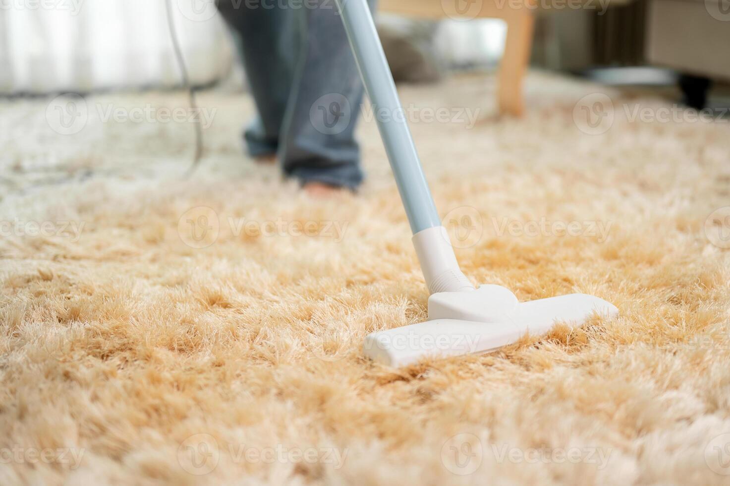 A close-up of a woman is vacuuming the carpet in the living room at home. image with a copy space photo