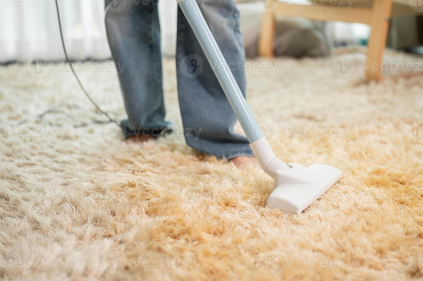 A close-up of a woman is vacuuming the carpet in the living room at home. image with a copy space photo