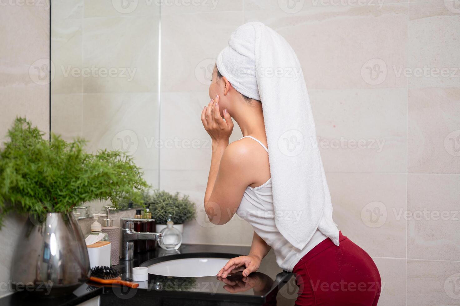 A beautiful Asian woman is touching her face and looking into the mirror in the bathroom. photo
