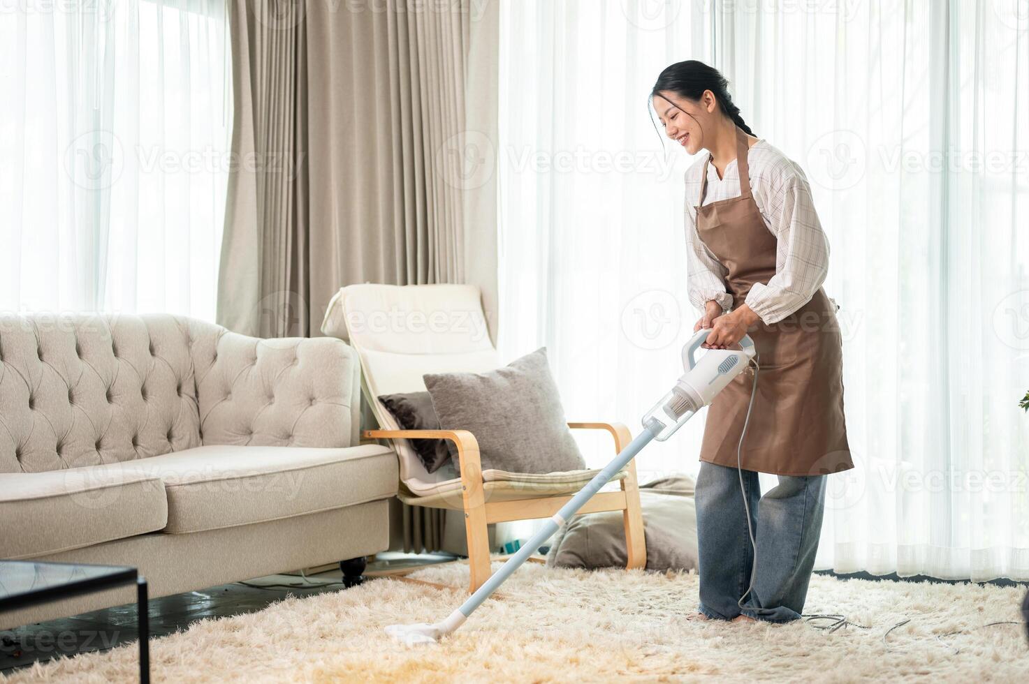 A beautiful Asian woman is cleaning a carpet with a vacuum cleaner in the living room at home. photo