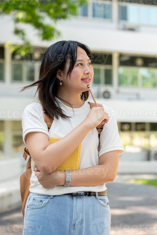 A pretty, thoughtful Asian female college student stands on her college campus, ponders some ideas. photo