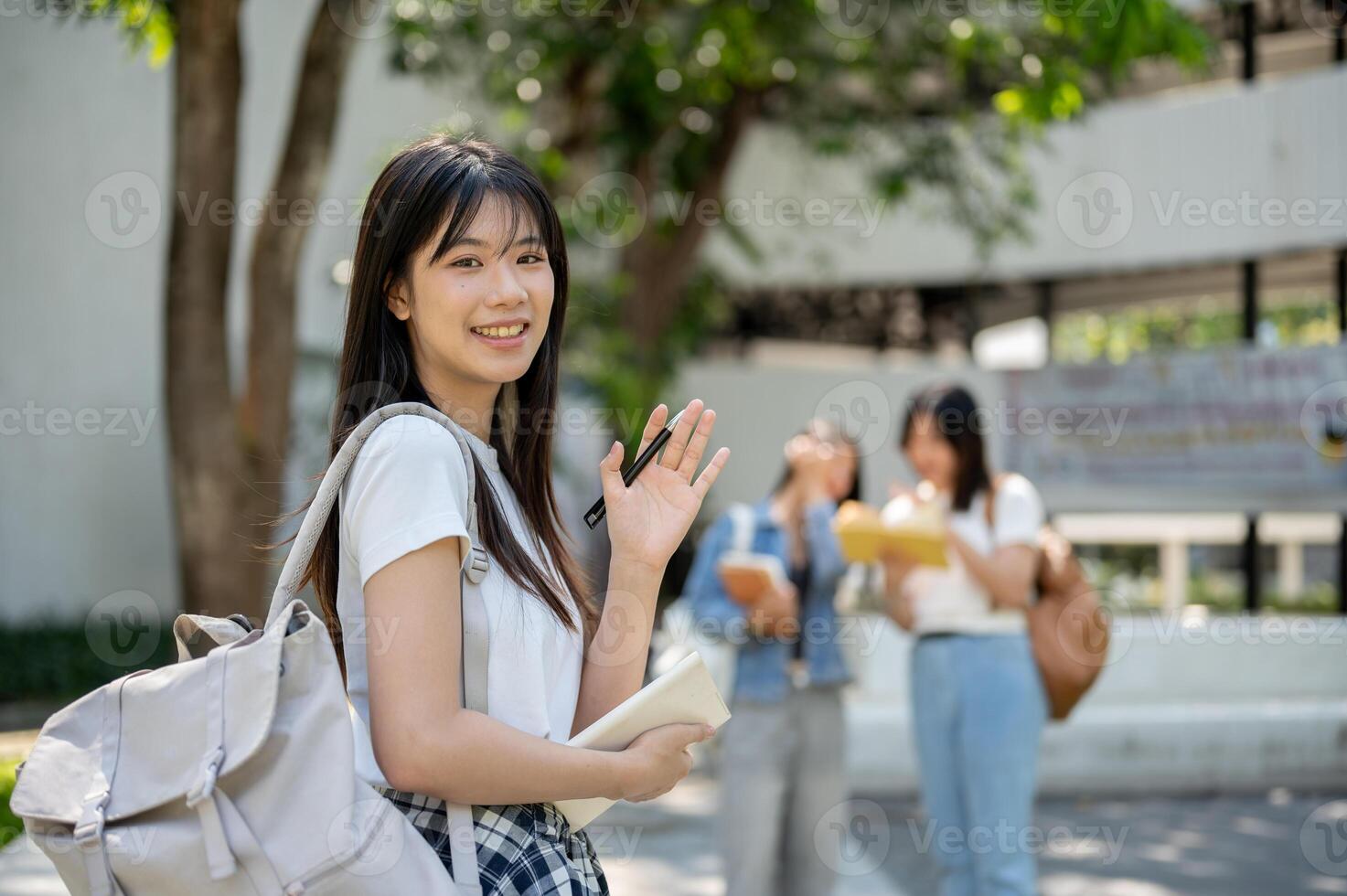 A friendly female student smiles and waves her hand at the camera while standing in her college park photo