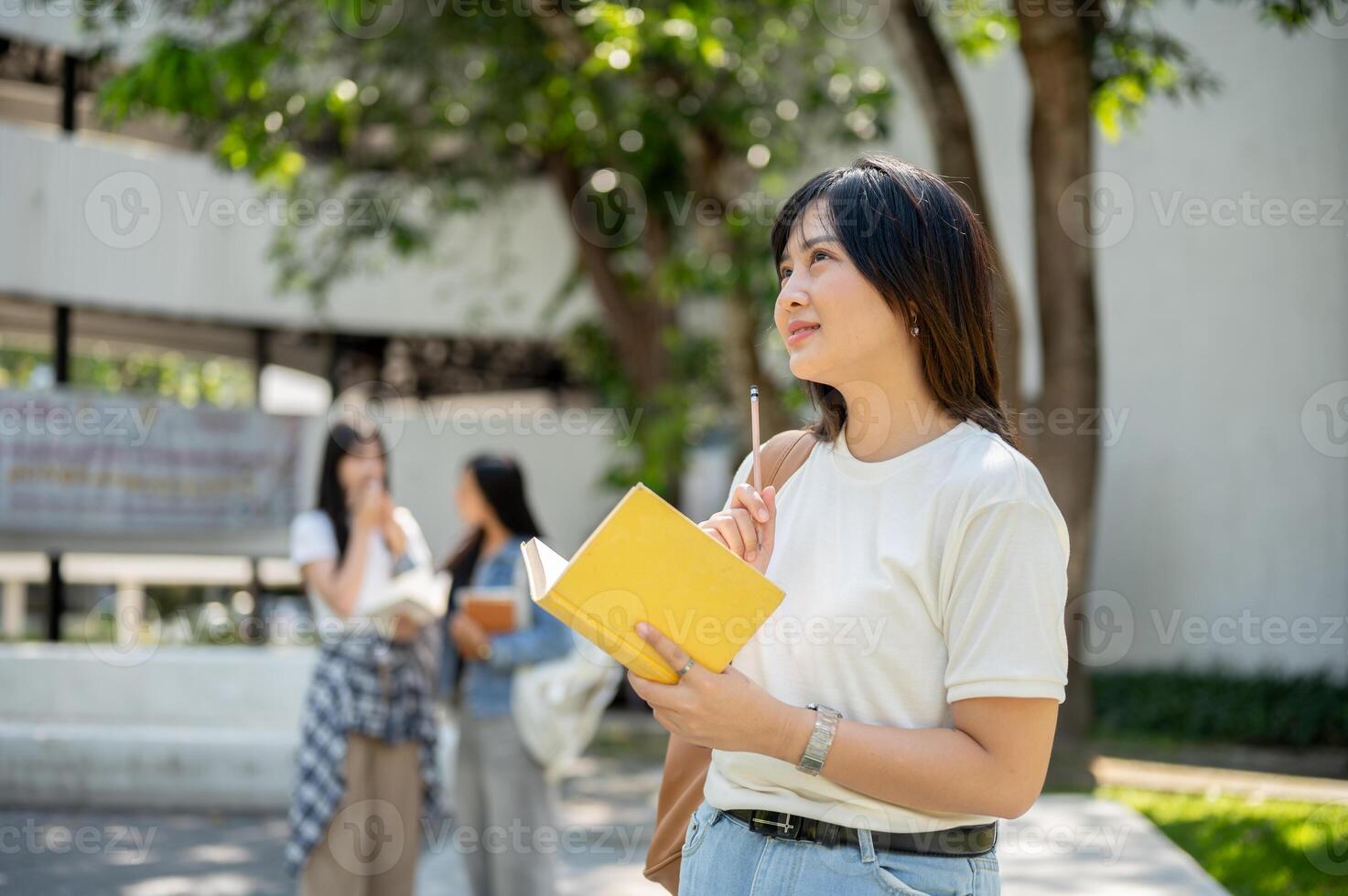 A pretty Asian female college student stands in a college park, looking away as if daydreaming. photo