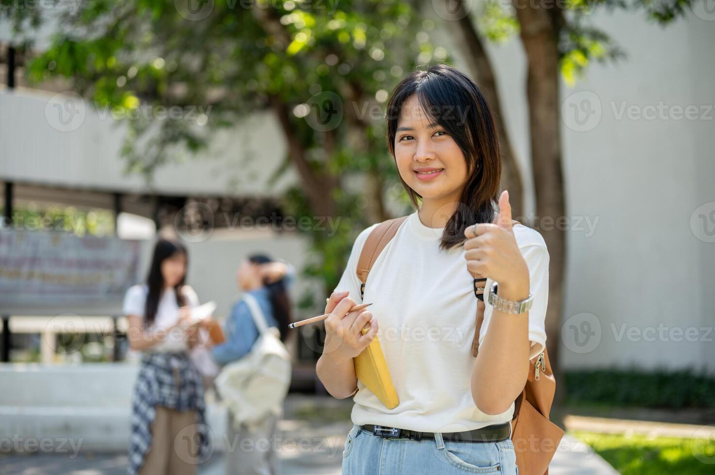 A female college student stands in her college park, smiling and giving a thumbs-up to the camera. photo