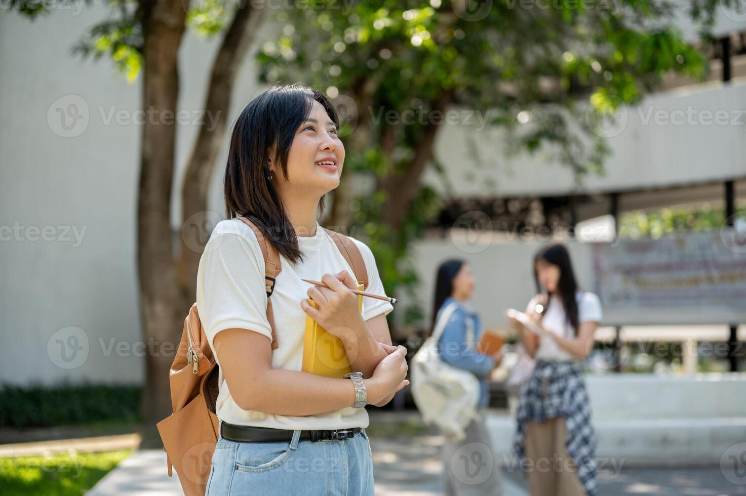 A pretty Asian female college student stands in a college park, looking away as if daydreaming. photo
