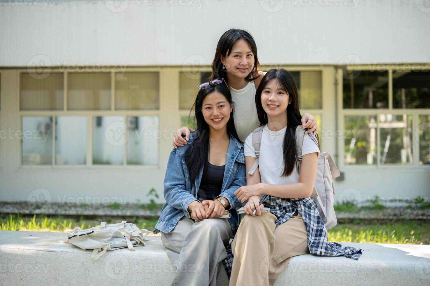 A group of Asian students is sitting on a bench in their college park, smiling at the camera. photo