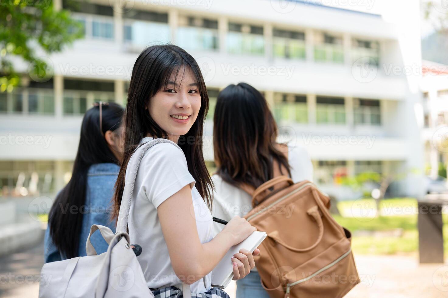 A happy Asian female college student is on the way to class with her friends, smiling at the camera. photo