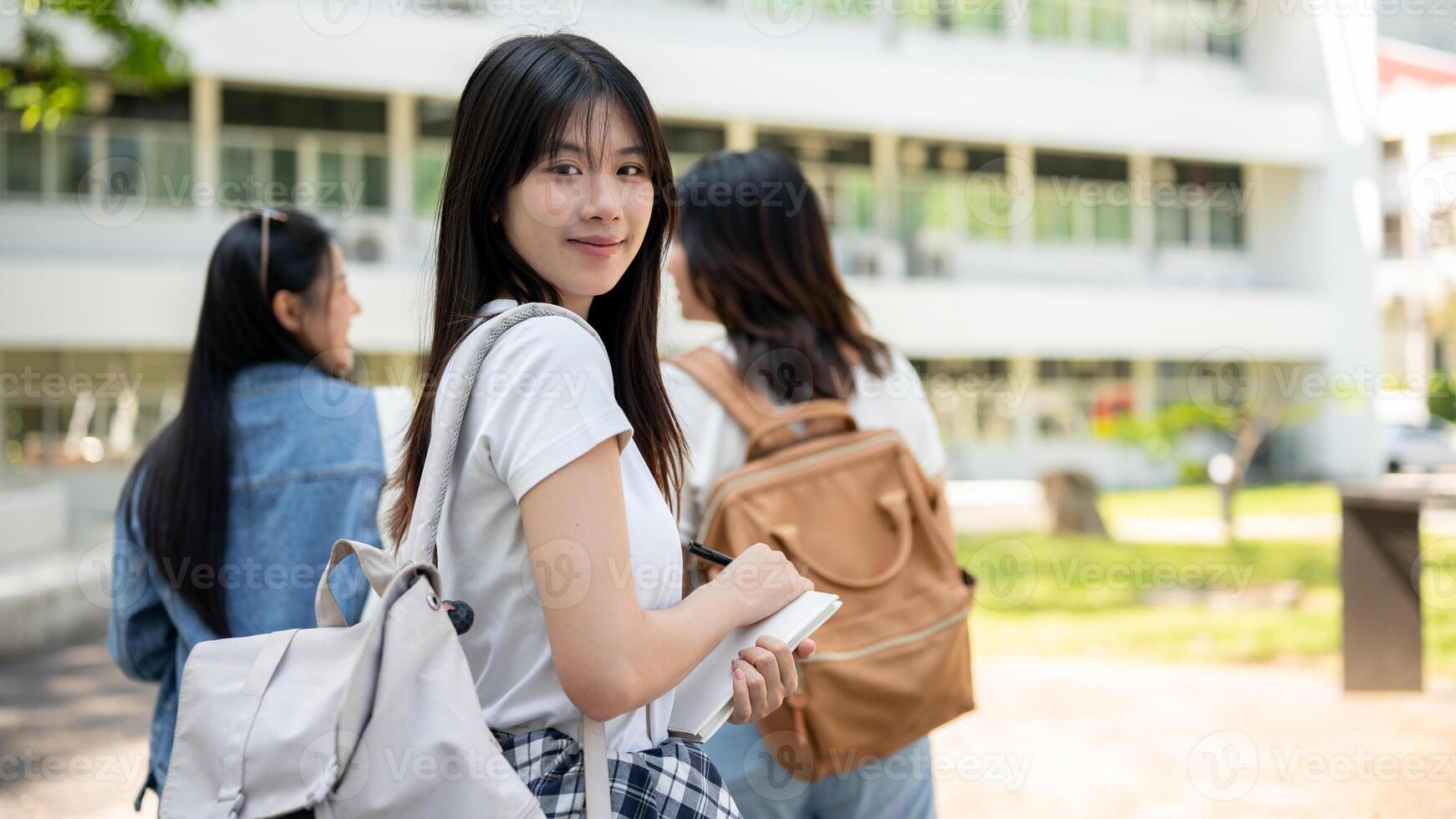 A happy Asian female college student is on the way to class with her friends, smiling at the camera. photo