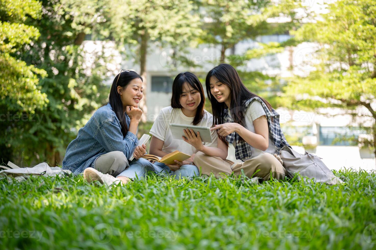 A group of students sits on the grass, chatting about a they're watching together on a tablet. photo