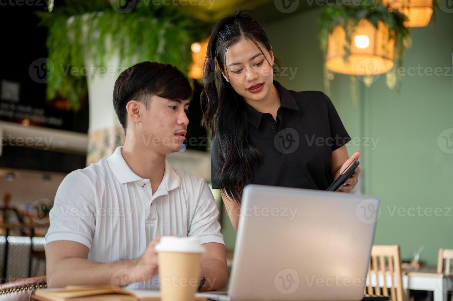 Two focused Asian colleagues are looking at a tablet screen, discussing its content, brainstorming. photo