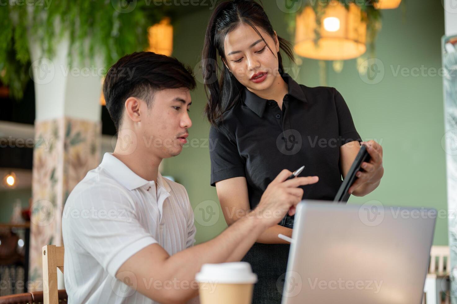 Two focused Asian colleagues are looking at a tablet screen, discussing its content, brainstorming. photo