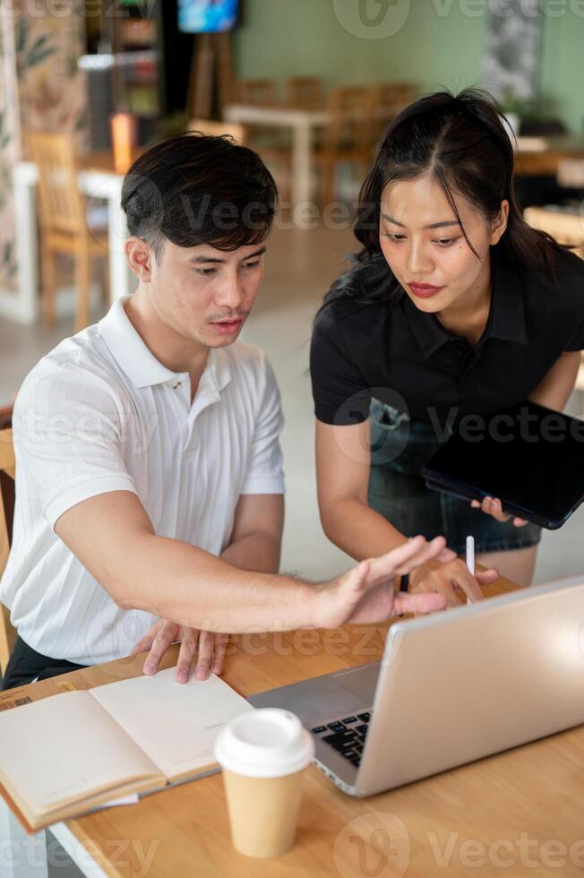 Two focused Asian colleagues are looking at a laptop screen, discussing its content, brainstorming. photo