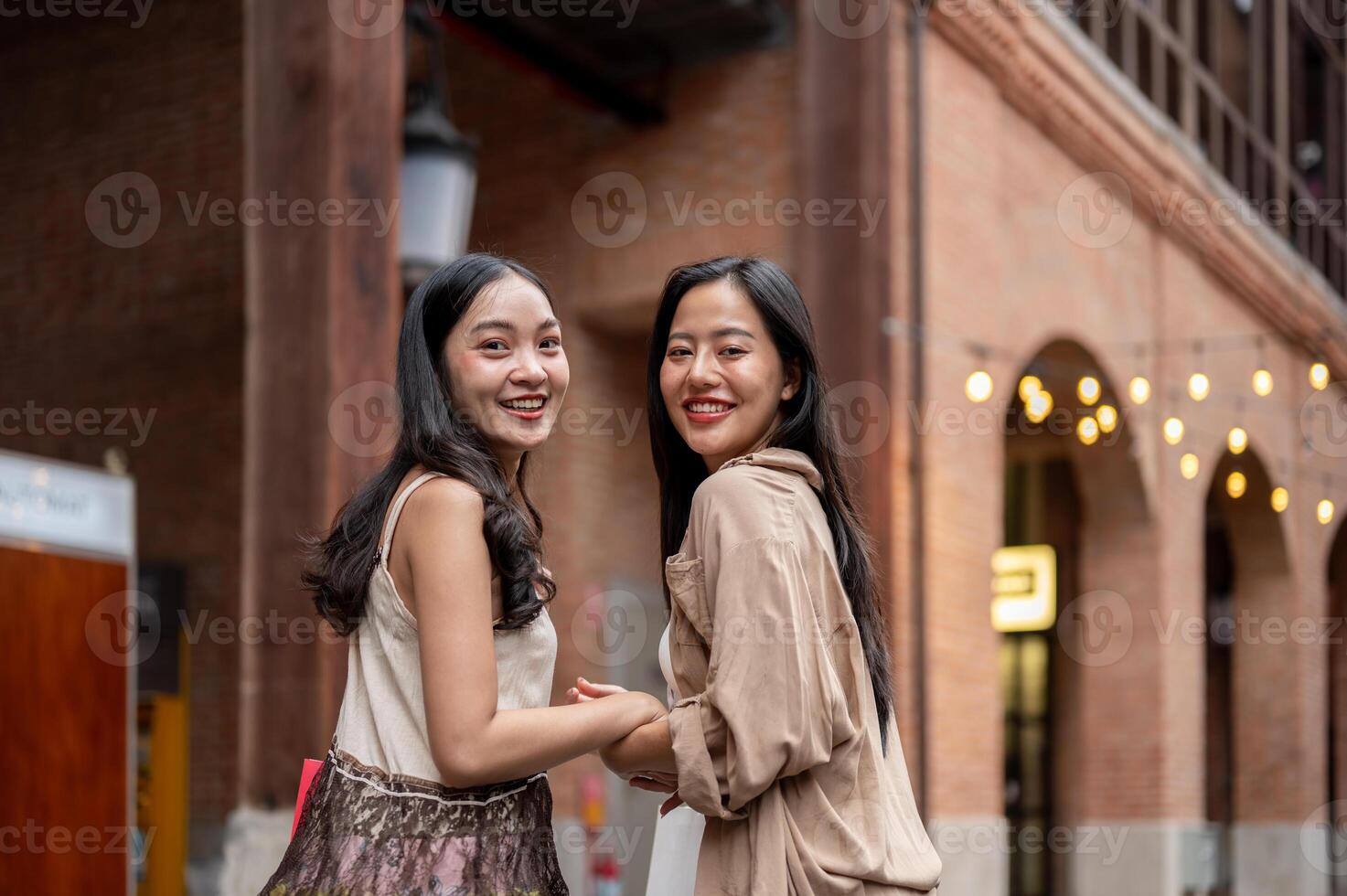 Two beautiful Asian female friends enjoy shopping together in the city, smiling at the camera. photo