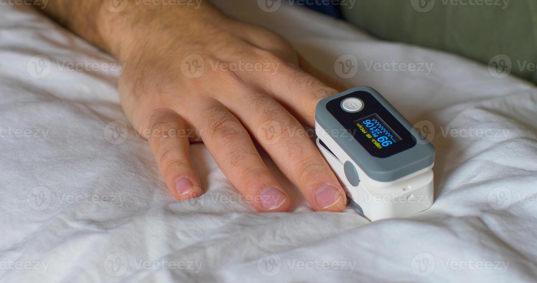 A person laying in bed with a finger on a pulse oximeter photo