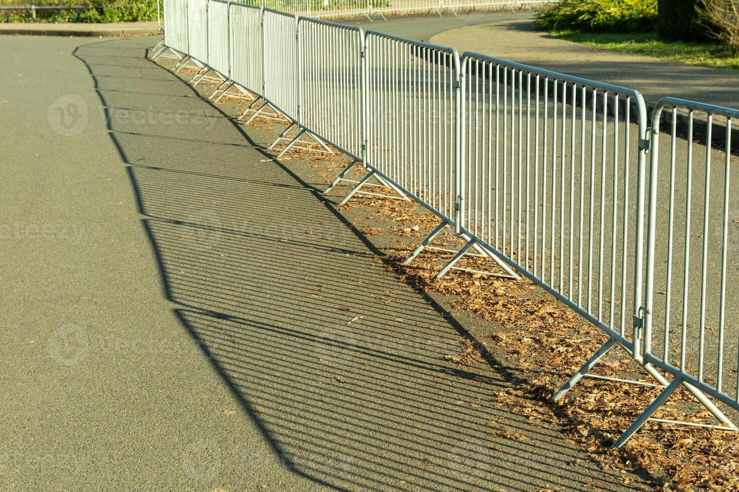 Long metal crowd control barriers casting shadows on asphalt road photo