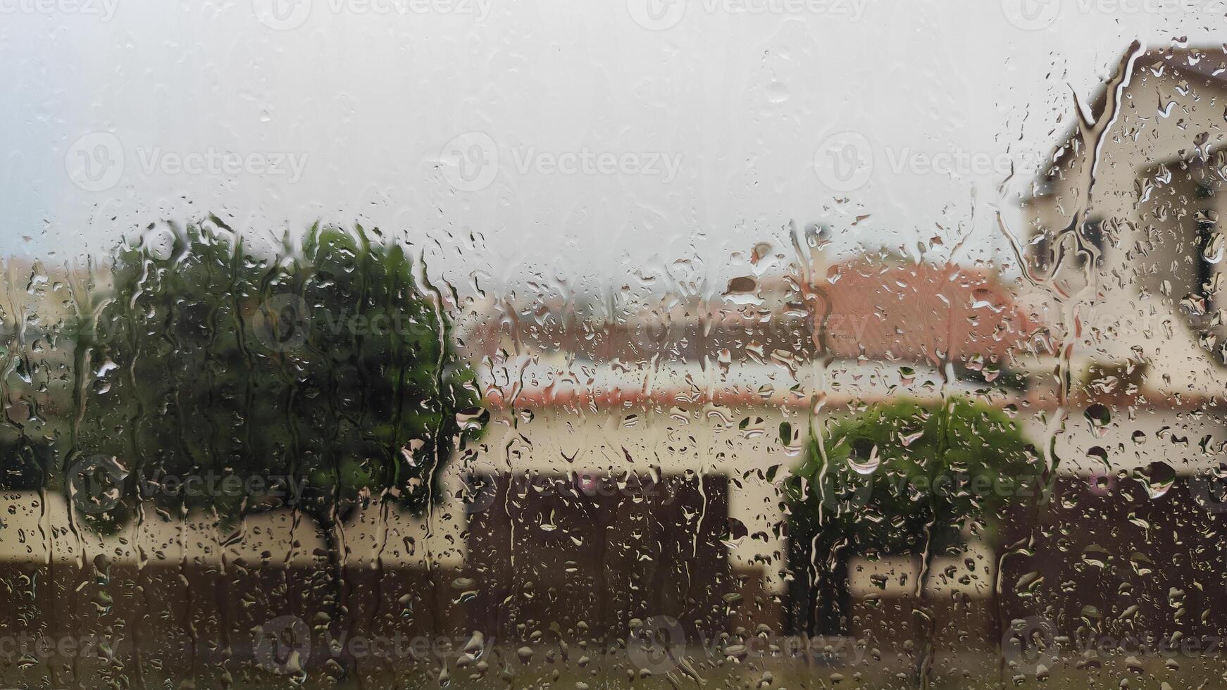Rain-covered window view of a suburban neighborhood with blurred background photo