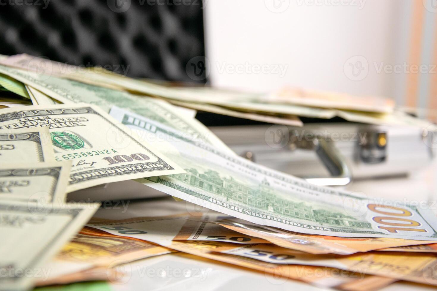 A close-up shot of several US dollar bills spread out on a white surface near a silver case. The bills are in various denominations and some are out of focus photo