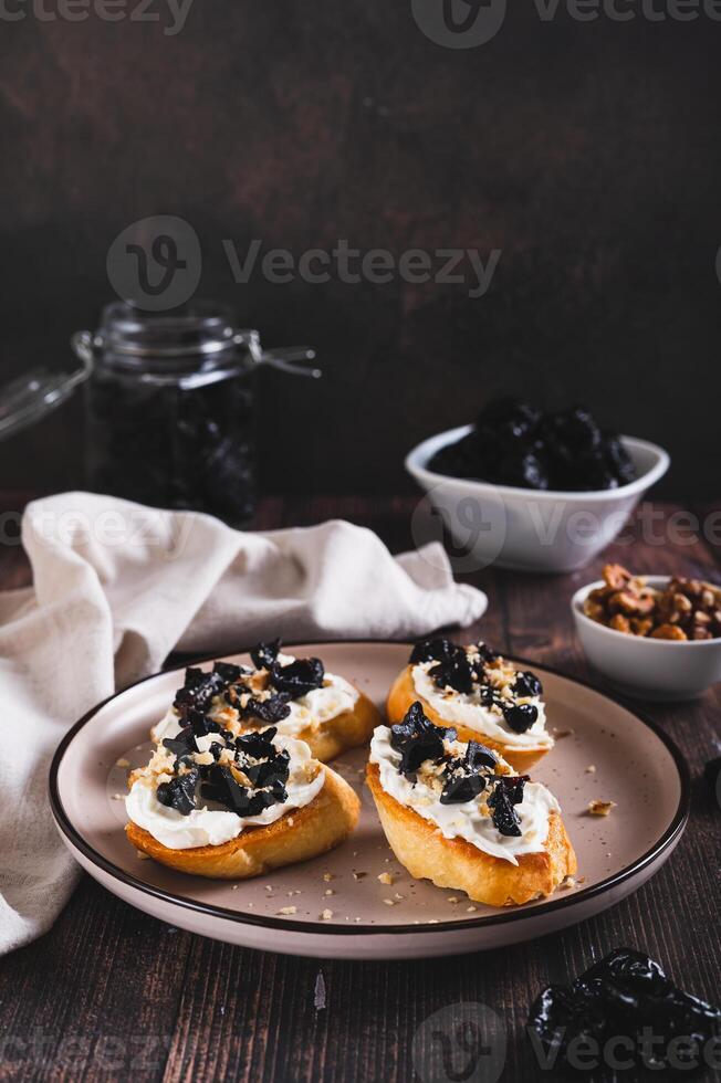 Delicious toasts with ricotta and prunes on a plate on the table web banner vertical view photo