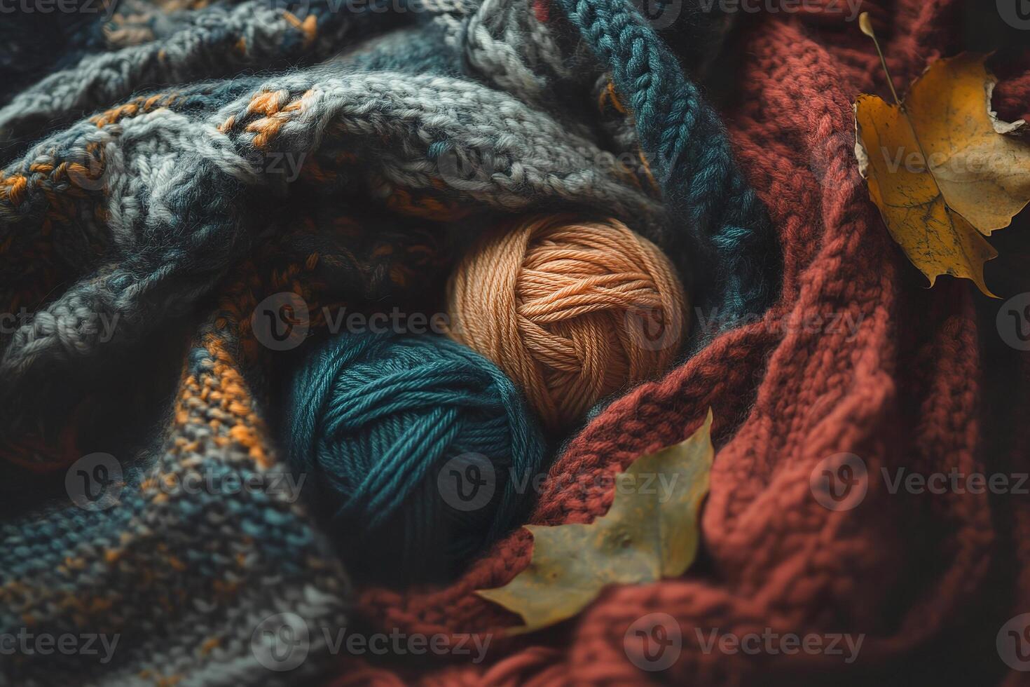 Bright, colorful yarn lays wrapped in a knitted blanket with autumn leaves around it photo
