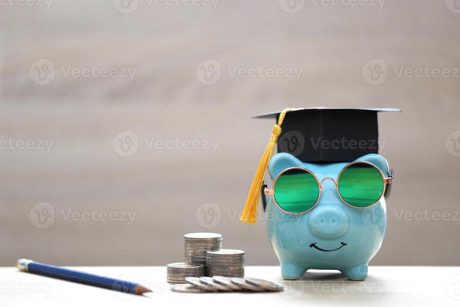 Graduation hat on blue piggy bank with stack of coins money on wooden background, Saving money for education concept photo