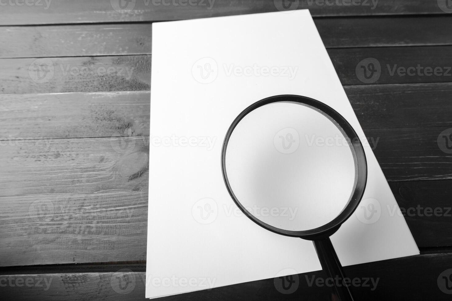 Magnifying glass and blank paper on wooden table photo