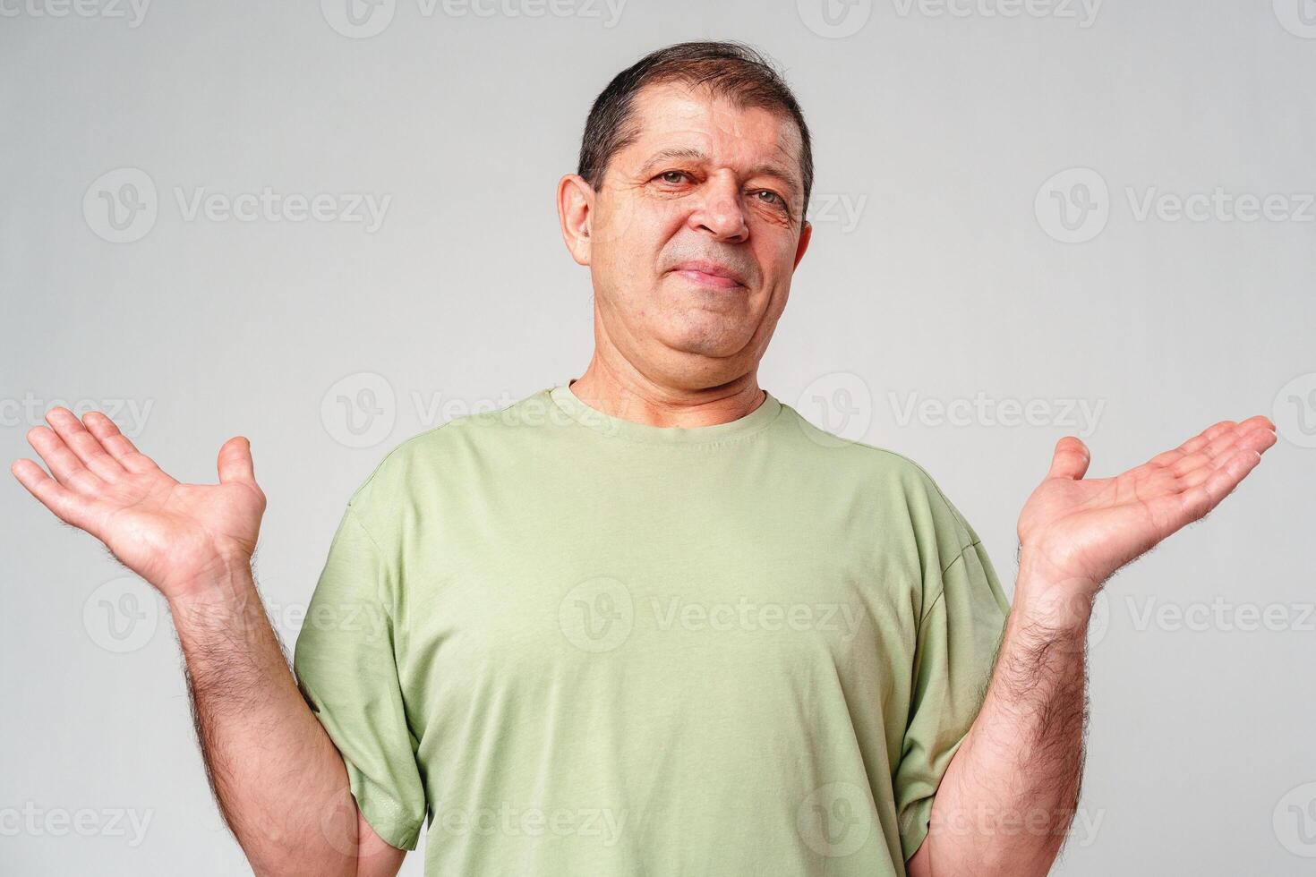 A middle-aged man with a neutral expression raises his hands in a questioning gesture against a plain backdrop photo