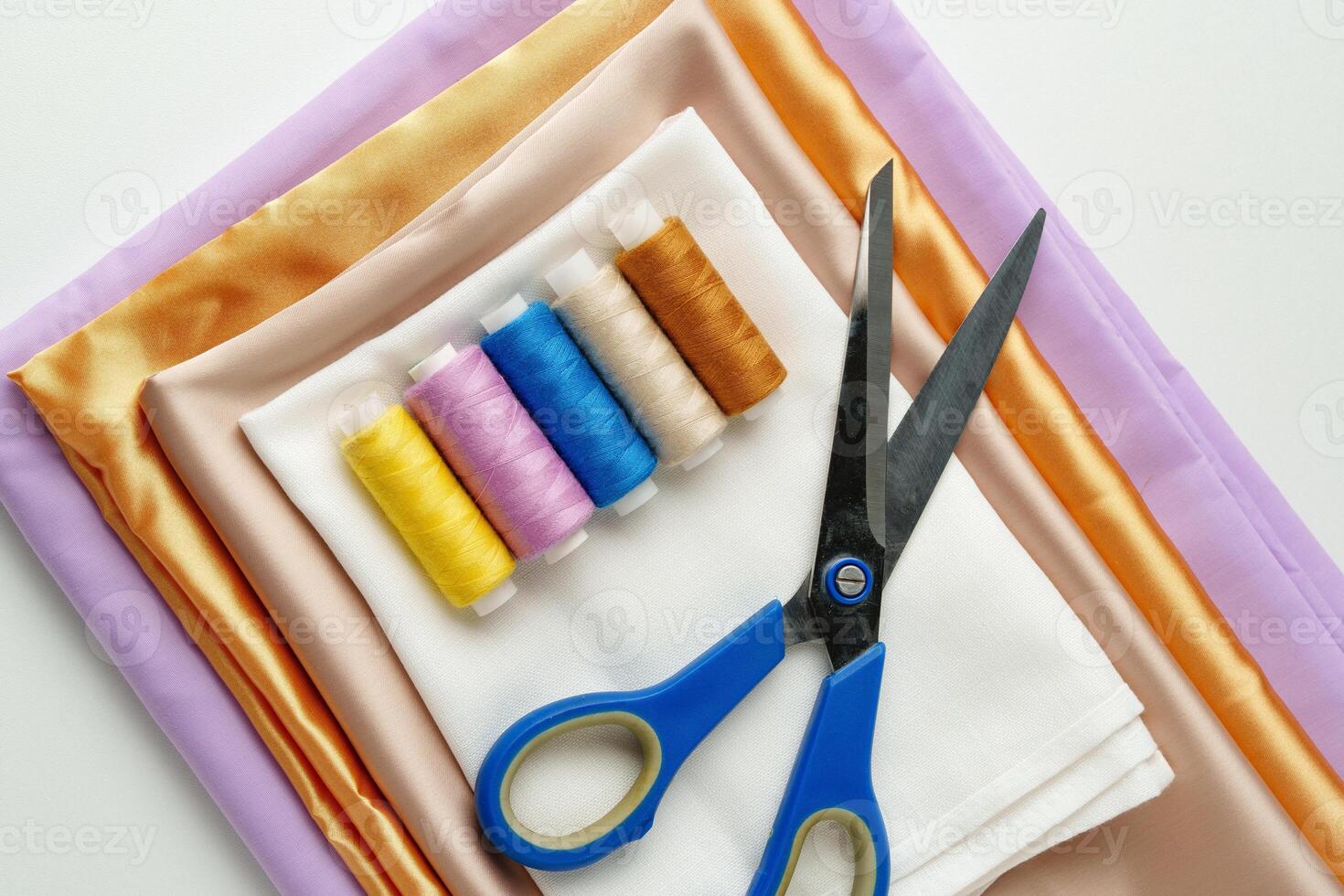 Colorful sewing threads and scissors placed next to folded fabrics in a craft workspace photo